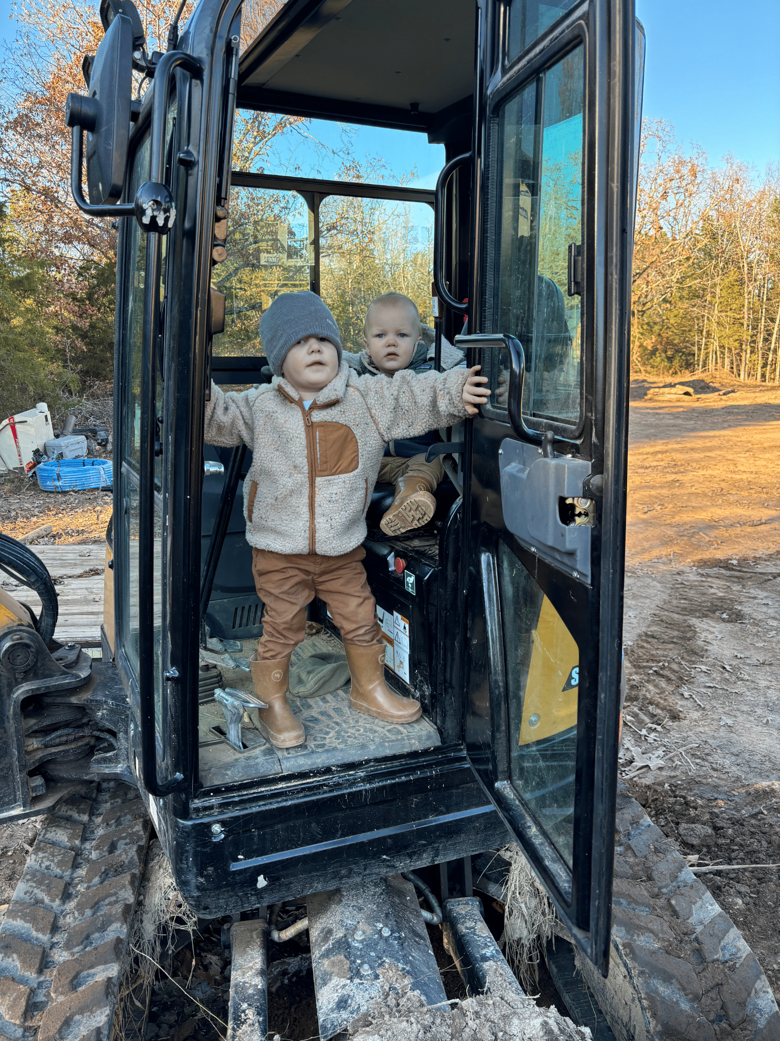 Two children standing in the cabin of a black excavator.