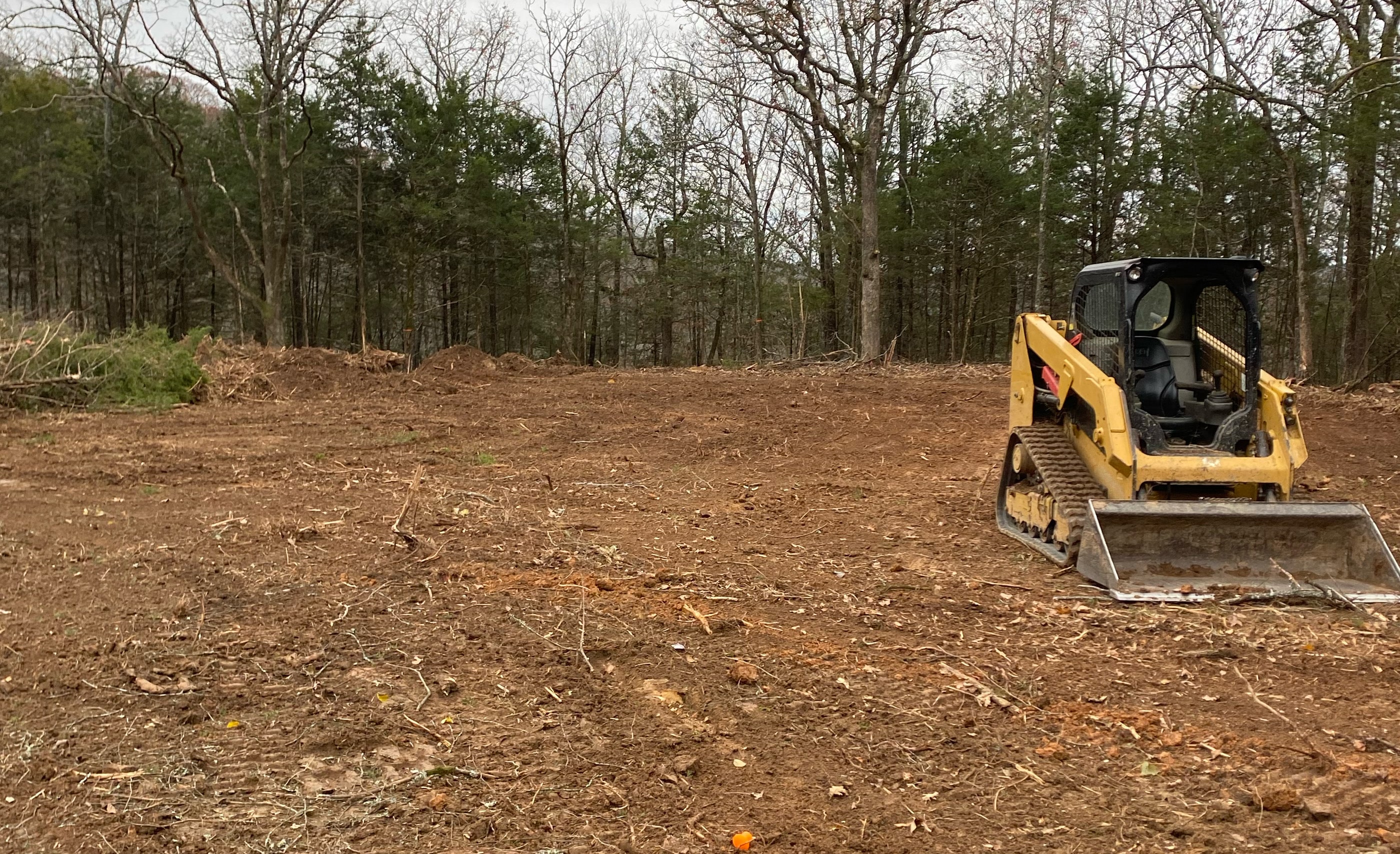 A yellow bulldozer positioned on a cleared area of land with trees in the background.