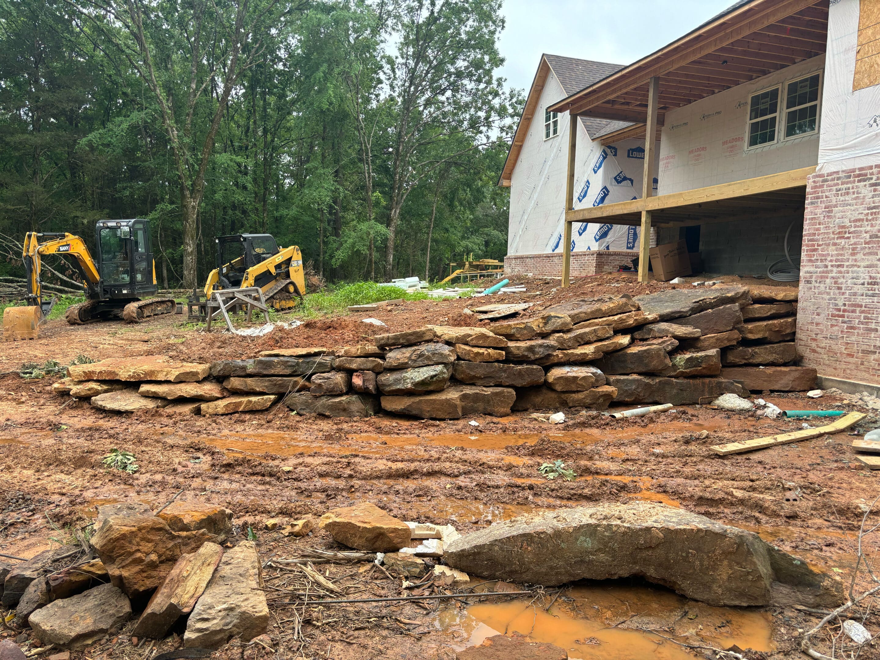 Construction site featuring large rocks and two pieces of machinery on a muddy surface.