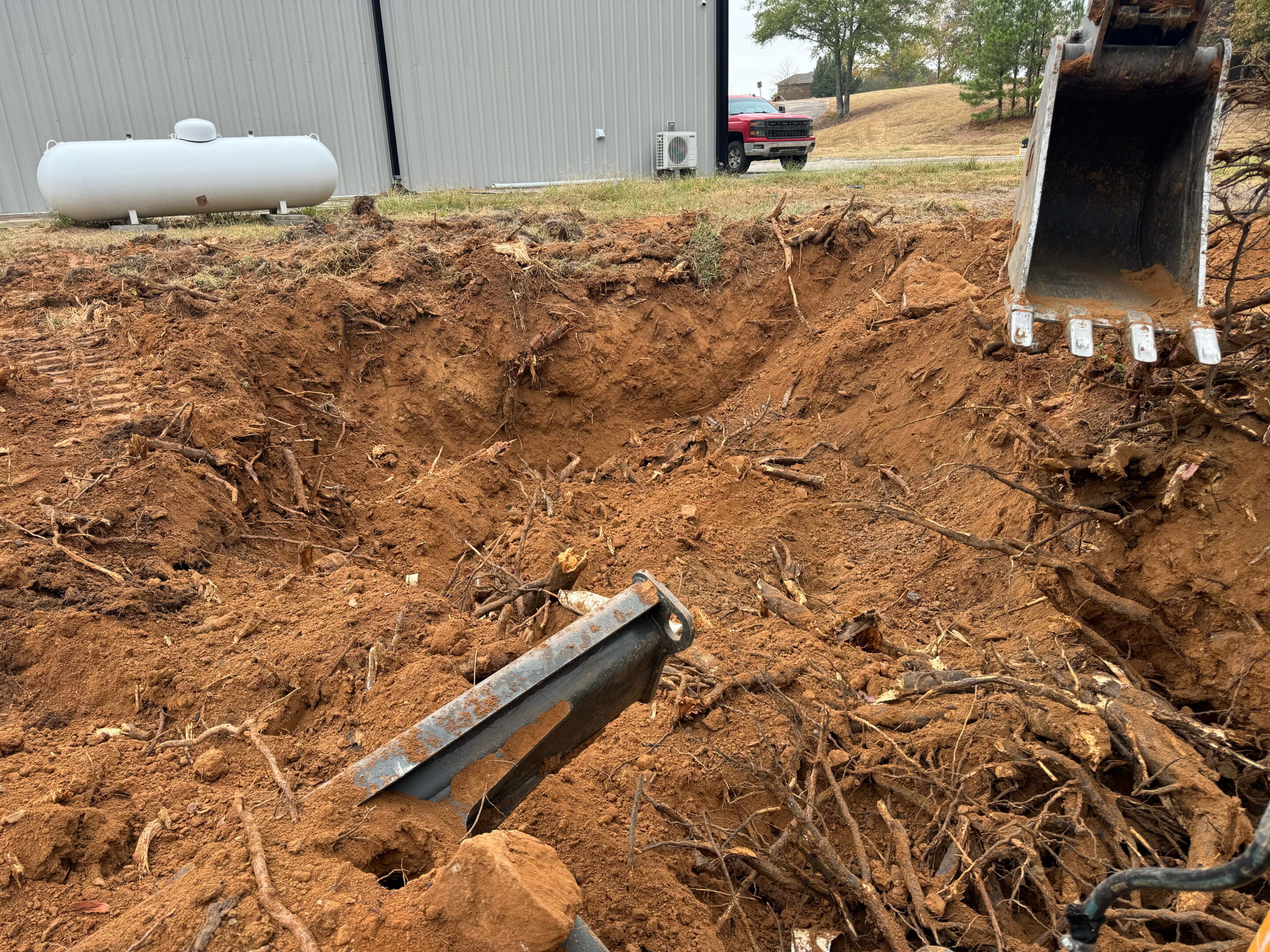 Excavated soil pit showing dirt and tree roots with machinery in the foreground.