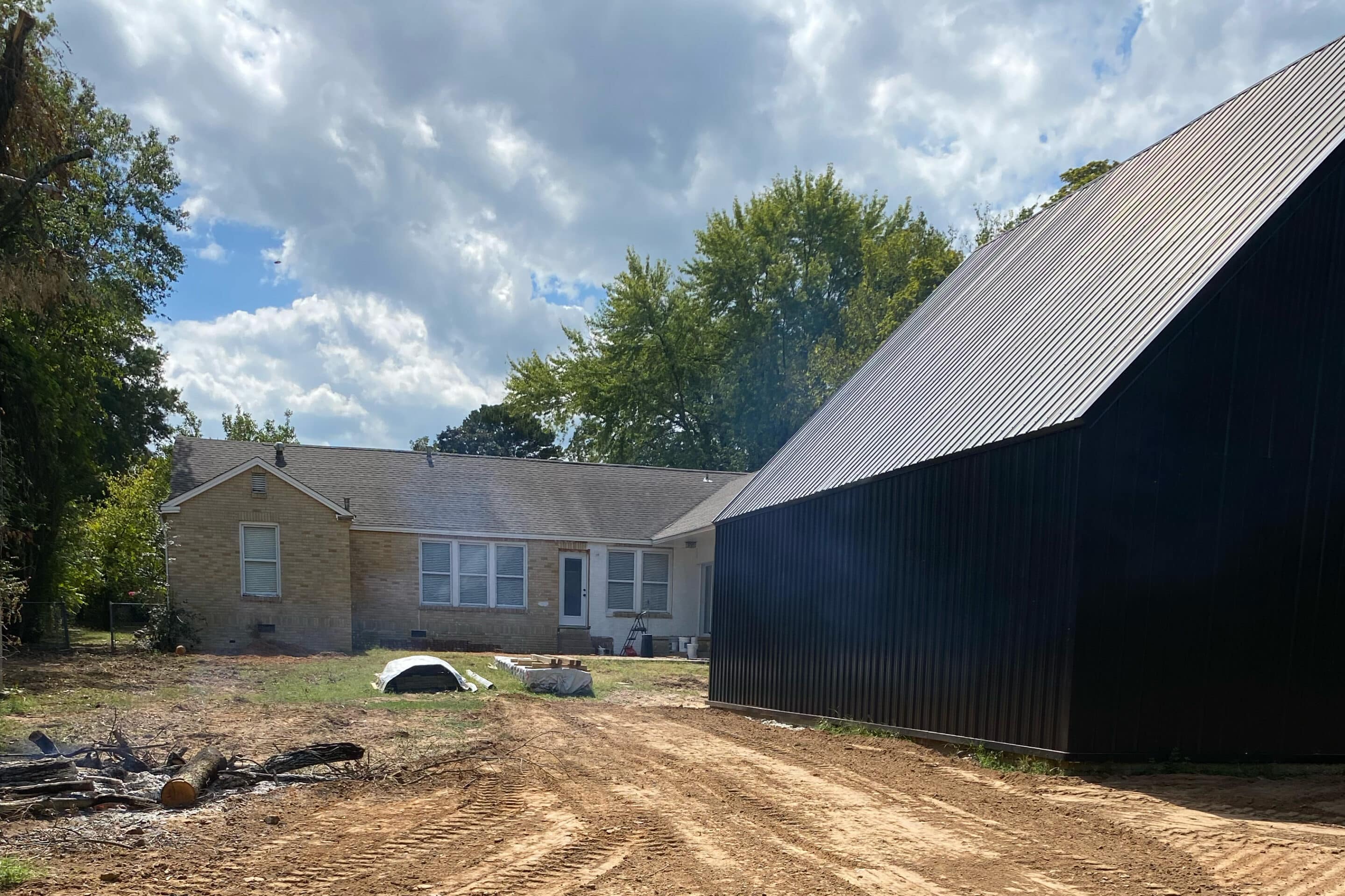 A residential building with a barn structure nearby on a cleared land area.